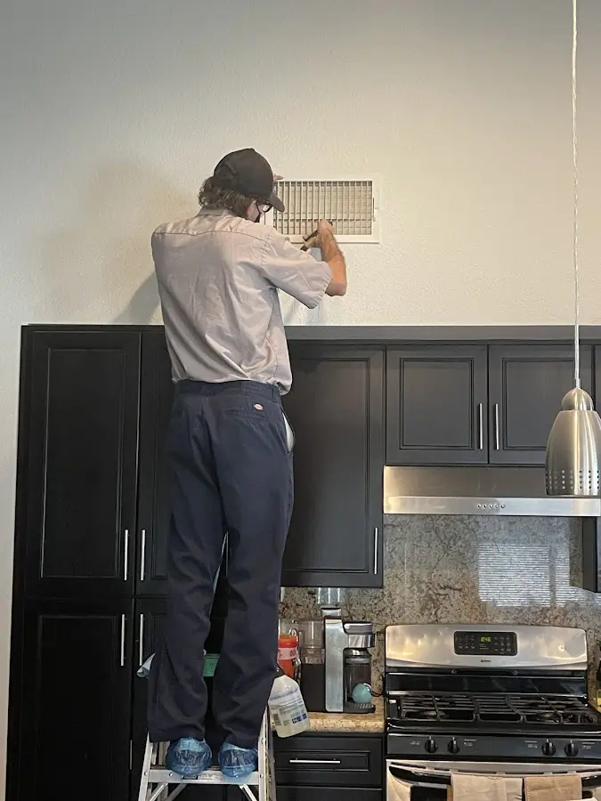 Technician inspecting an air vent during HVAC service in Holiday